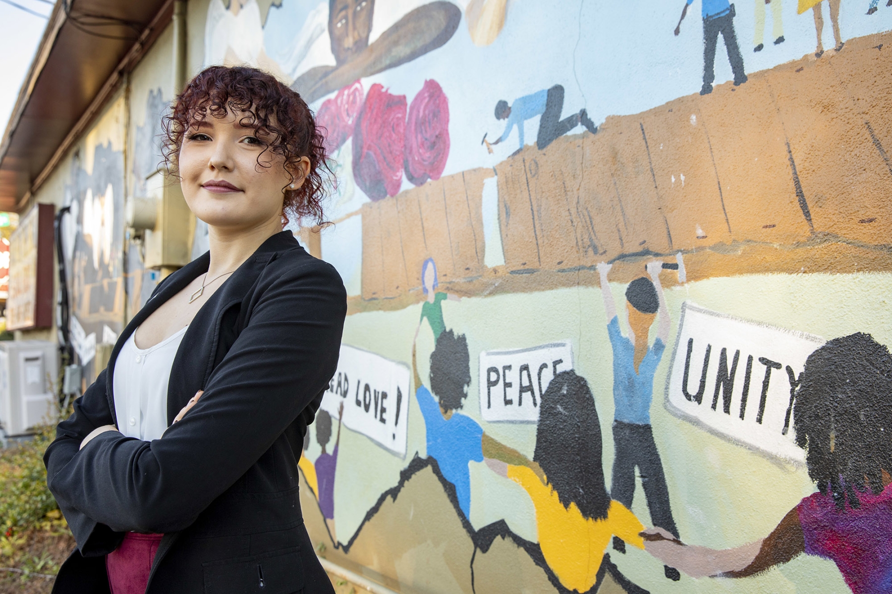 Environmental portrait of undergraduate student Allison Reid at the Building Bridges mural on the Food for the Soul restaurant in Athens. The mural depicts the growth and improvement of police and community relations.