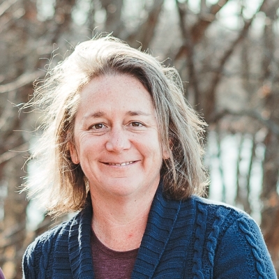 person in a blue sweater smiling in front of trees
