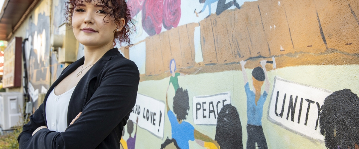 Environmental portrait of undergraduate student Allison Reid at the Building Bridges mural on the Food for the Soul restaurant in Athens. The mural depicts the growth and improvement of police and community relations.